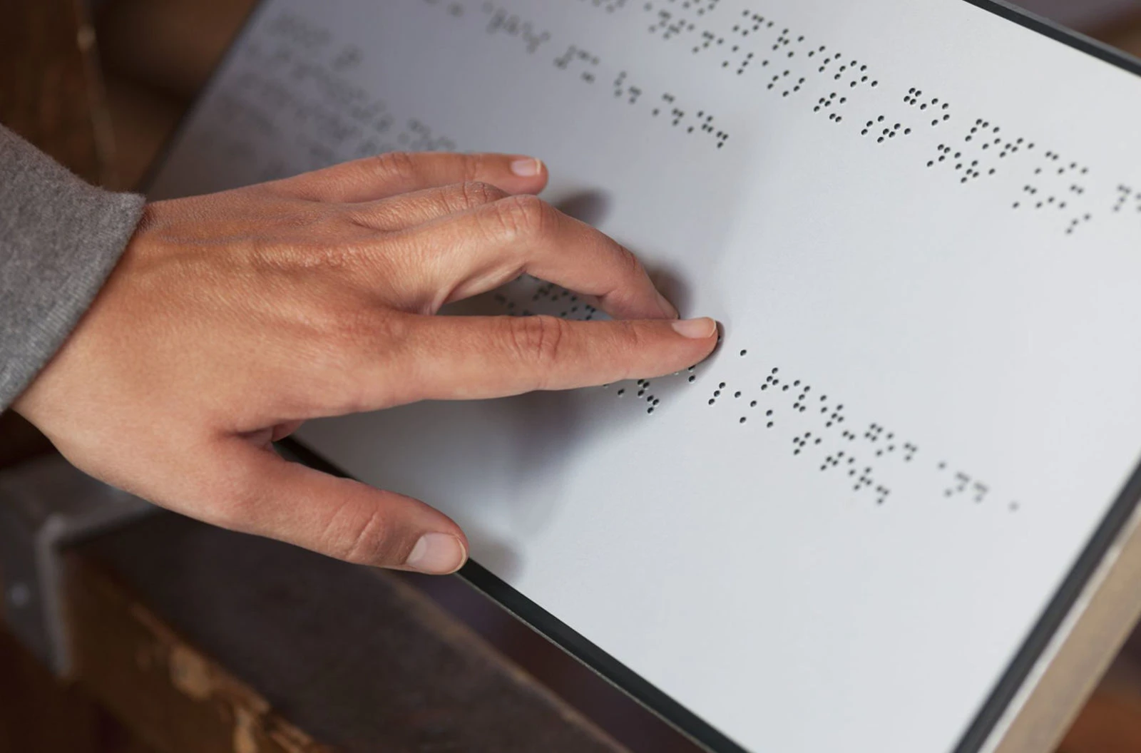 A person reading a braille sign by touch. The sign is an example of custom ADA signs designed for accessibility, featuring raised braille text for visually impaired users.