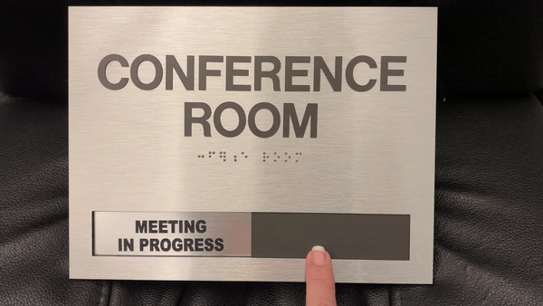 Conference room sign with braille and a slider indicating 'Meeting in Progress,' showcasing functional hospitality and hotel signage.