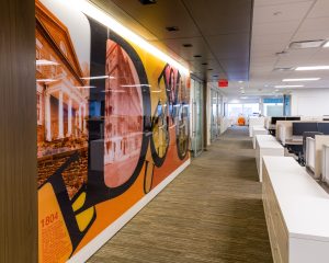 Long office hallway with a large, colorful Philadelphia-themed mural running the length of the wall, adjacent to open workstations and glass-walled offices.