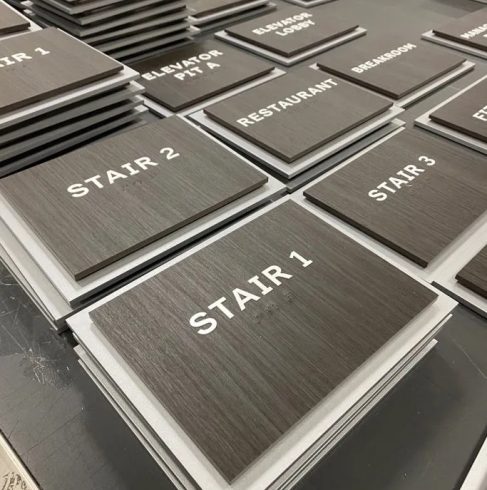 Stacks of directional and room signs labeled for stairs, elevators, and other facilities, representing hospitality and hotel signage